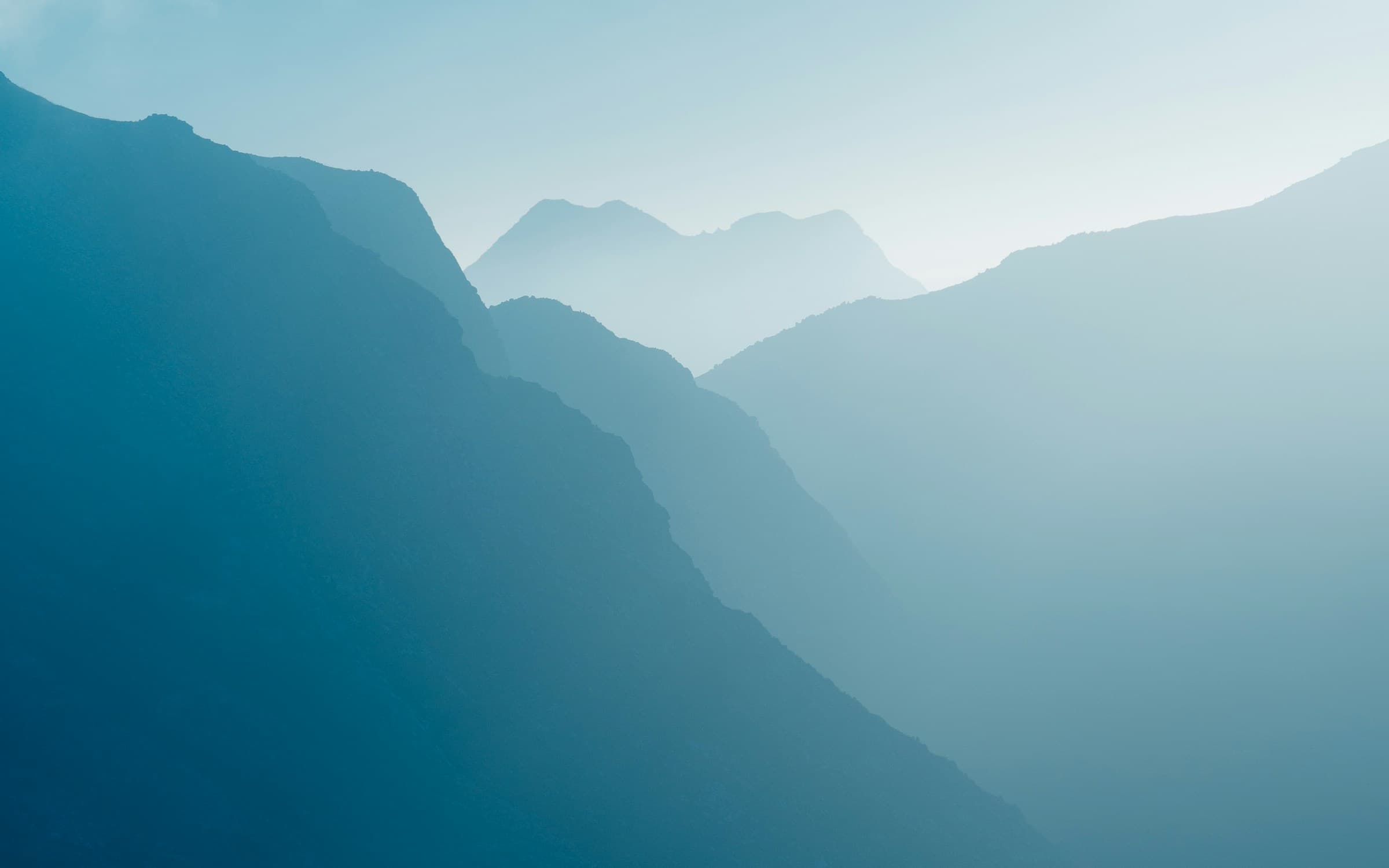 Layered mountain ridges resolving one by one out of morning fog.